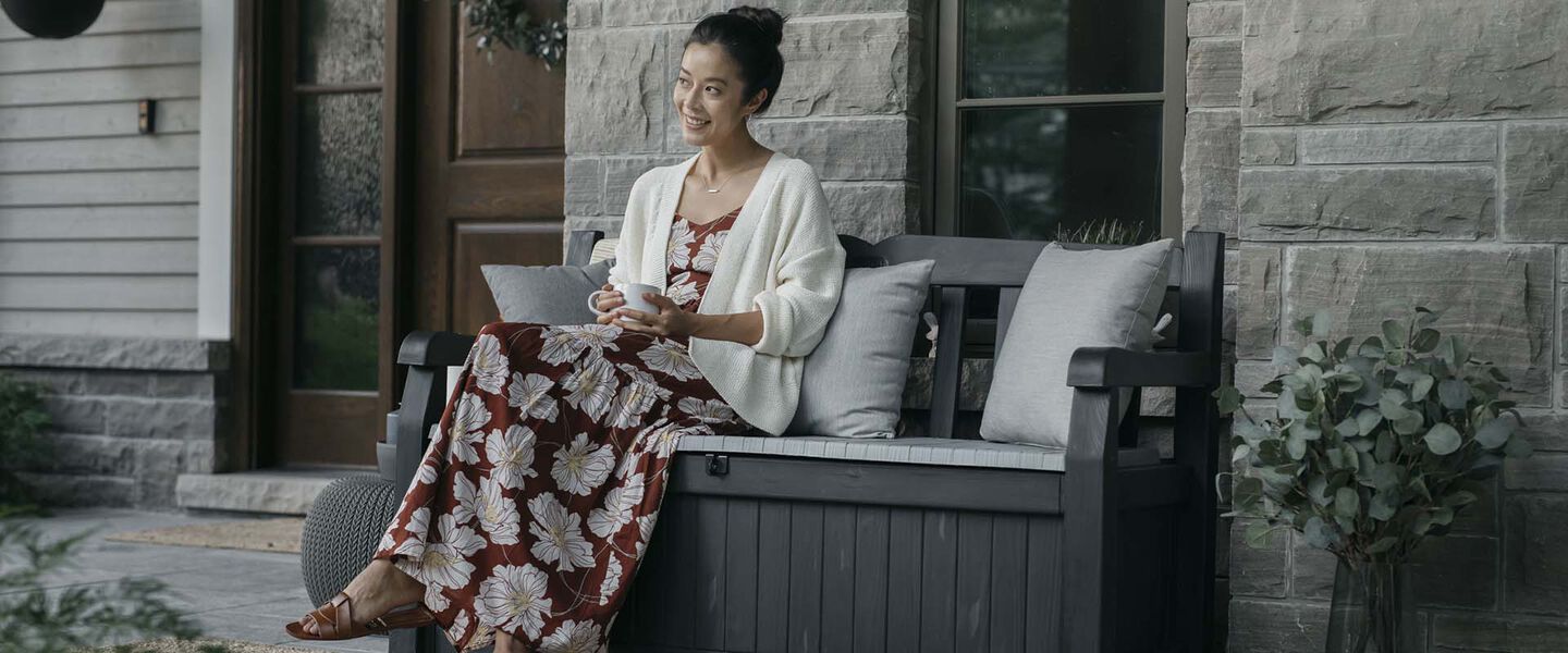 Woman on grey Keter outdoor storage bench Solana in front of house. 