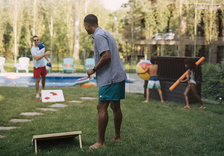 2 men playing corn hole next to the pool