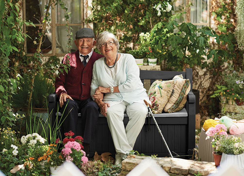 Un couple âgé est assis sur le banc Keter dans le jardin