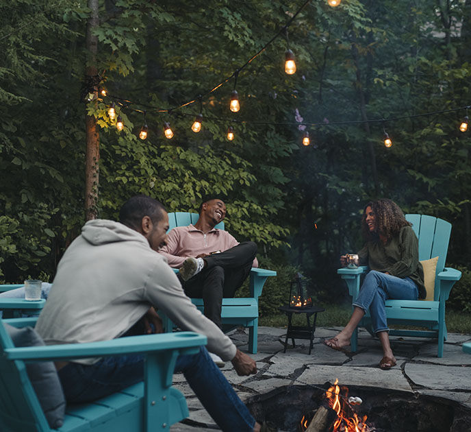 Trois amis autour d'un feu de joie grillant des guimauves assis sur des chaises Keter