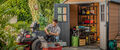 A man outside his open shed working on his lawnmower